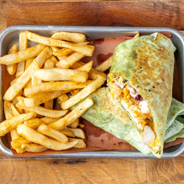A green wrap filled with chicken and vegetables, served with a side of golden french fries.
