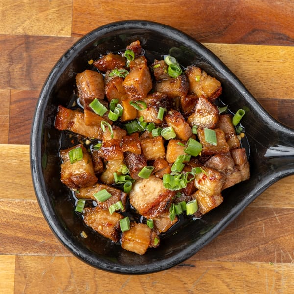 Close-up of glazed pork belly pieces topped with chopped green onions in a black dish.