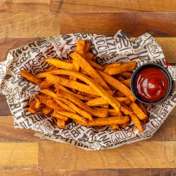 Sweet potato fries in a paper-lined basket with a side of ketchup on a wooden table.