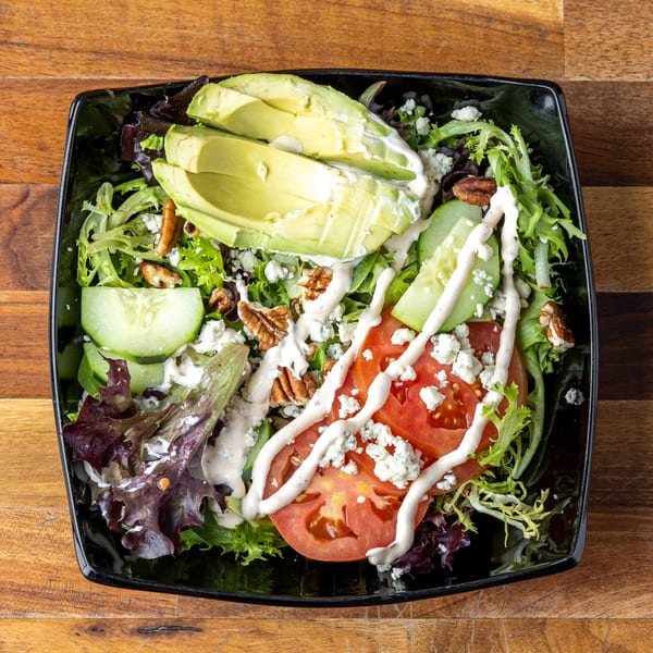 A vibrant salad with mixed greens, avocado, tomatoes, cucumbers, pecans, blue cheese, and ranch dressing.