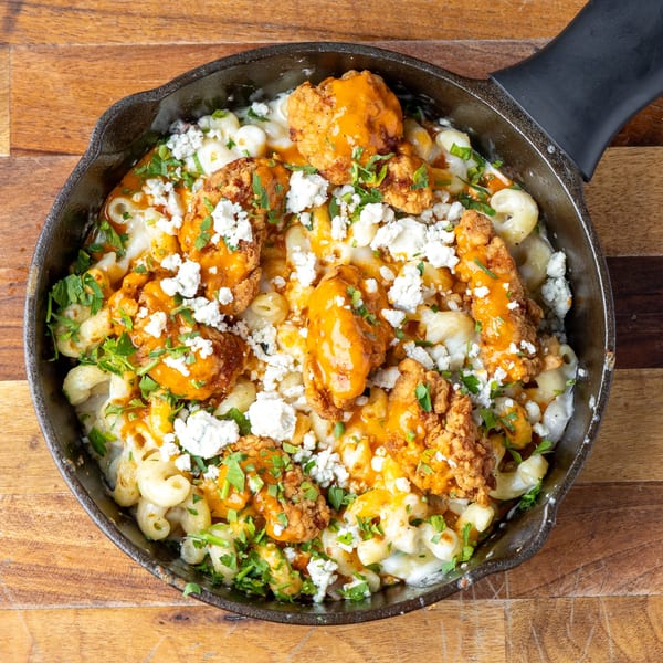 Buffalo chicken mac and cheese in a cast iron skillet, topped with blue cheese and parsley.