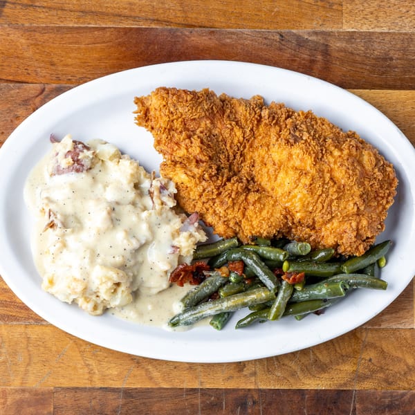 Crispy fried chicken, mashed potatoes with gravy, and green beans with bacon on a white plate.