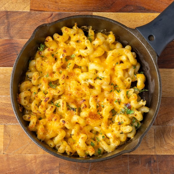 Baked macaroni and cheese with melted cheddar and parsley in a cast iron skillet.